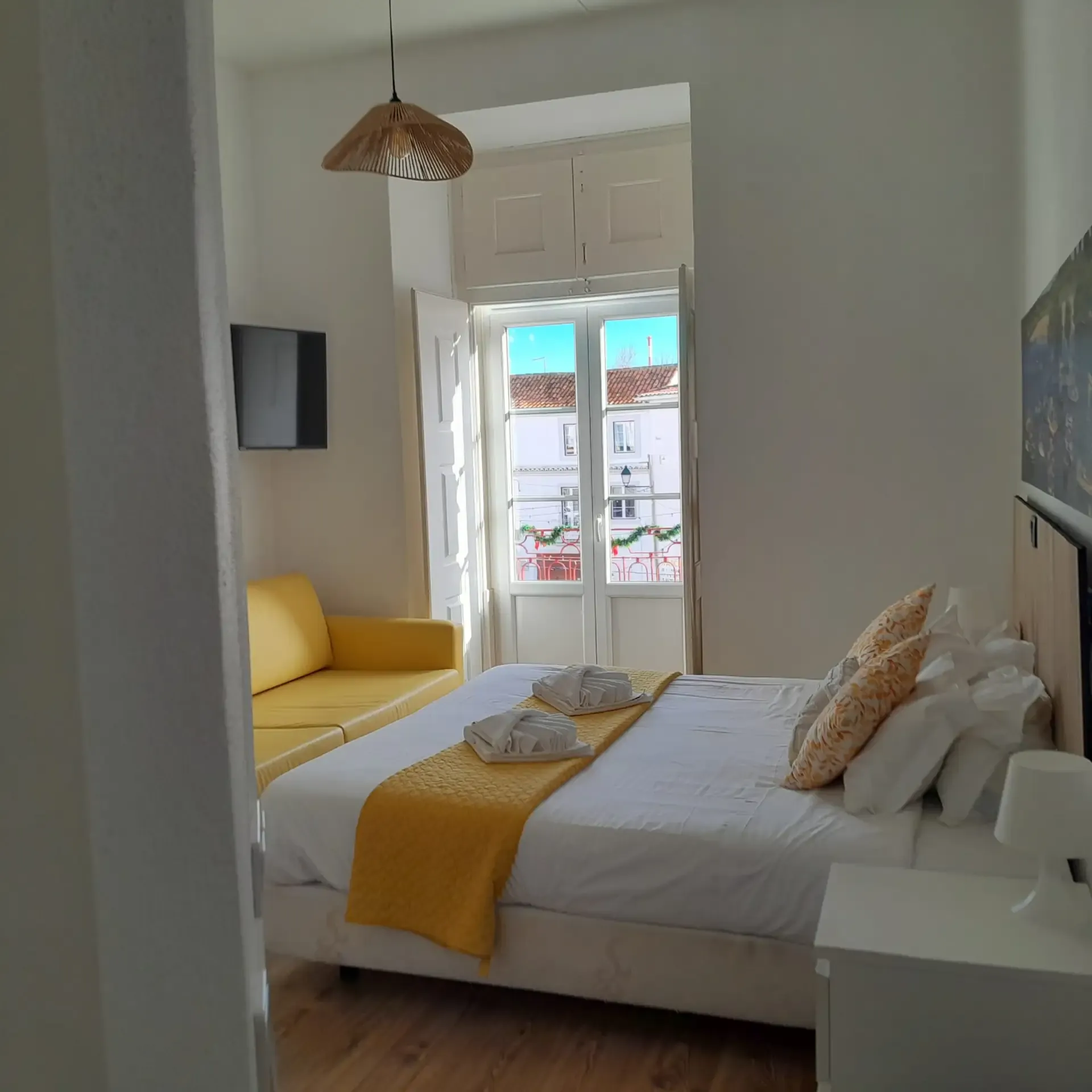 Deluxe room — yellow sofa, TV and balcony door onto the historic centre